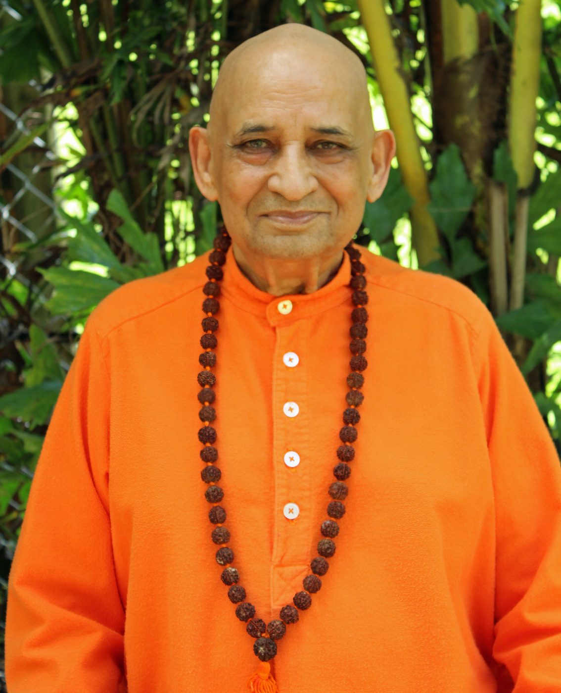 Sri Swami Jyotirmayananda standing in the ashram garden in South Miami, his rudraksha mala on, looking straight at the camera